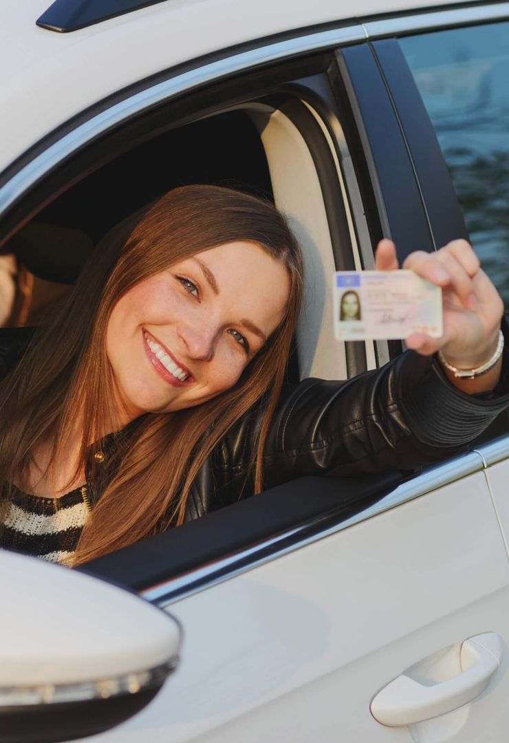 Eine Frau sitzt im Auto und zeigt ihren Führerschein